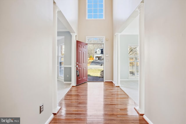 foyer featuring light wood-type flooring, ornate columns, a towering ceiling, and baseboards