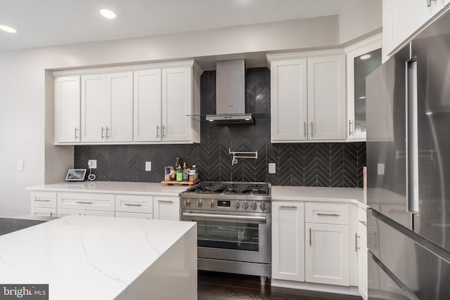 kitchen with light stone counters, stainless steel appliances, glass insert cabinets, white cabinets, and wall chimney range hood