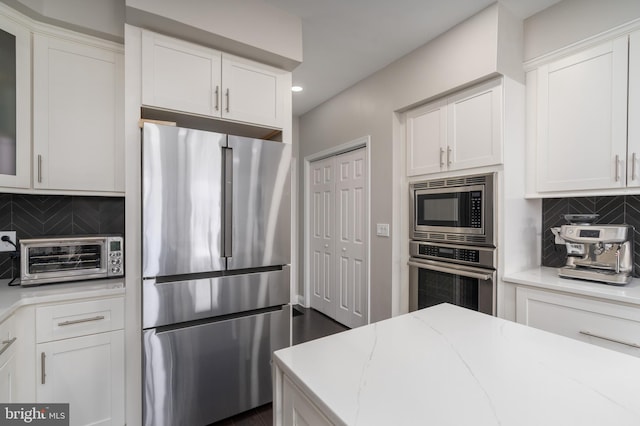 kitchen featuring light stone counters, a toaster, decorative backsplash, appliances with stainless steel finishes, and white cabinetry