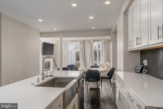 kitchen featuring light stone counters, a sink, white cabinetry, tasteful backsplash, and a glass covered fireplace