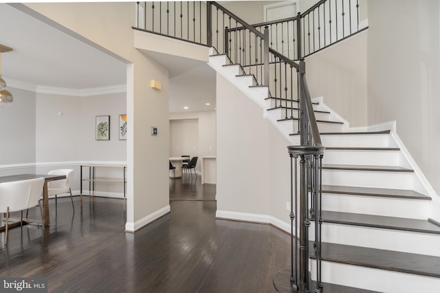 stairs with a towering ceiling, crown molding, baseboards, and wood finished floors