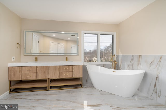 bathroom featuring a freestanding bath, marble finish floor, double vanity, and a sink