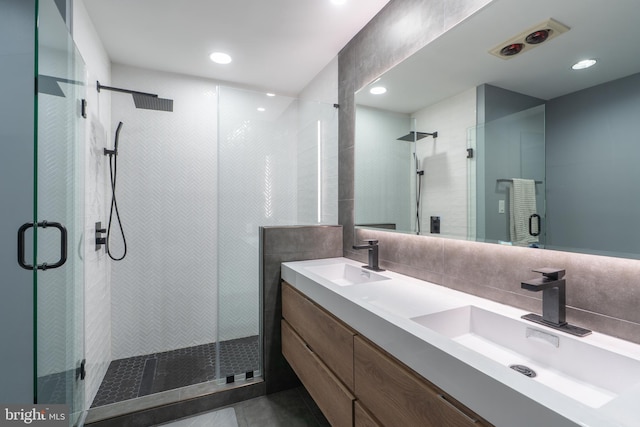 full bath featuring double vanity, a stall shower, tasteful backsplash, and a sink