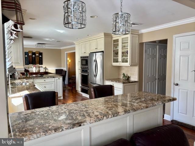 kitchen featuring cream cabinetry, stainless steel appliances, ornamental molding, a chandelier, and a peninsula