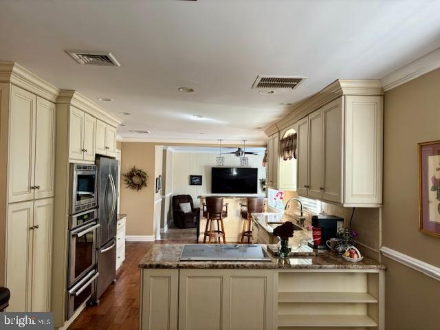 kitchen featuring dark stone counters, stainless steel appliances, cream cabinets, and visible vents