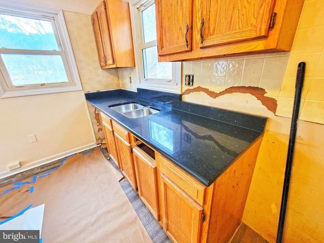 kitchen featuring brown cabinetry, dark countertops, a sink, and backsplash