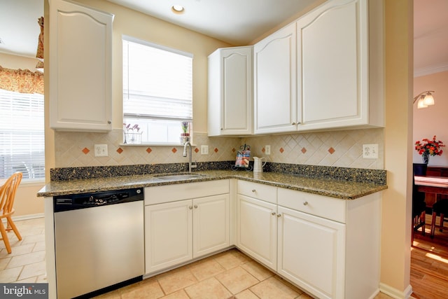 kitchen with a sink, white cabinets, stainless steel dishwasher, decorative backsplash, and dark stone countertops