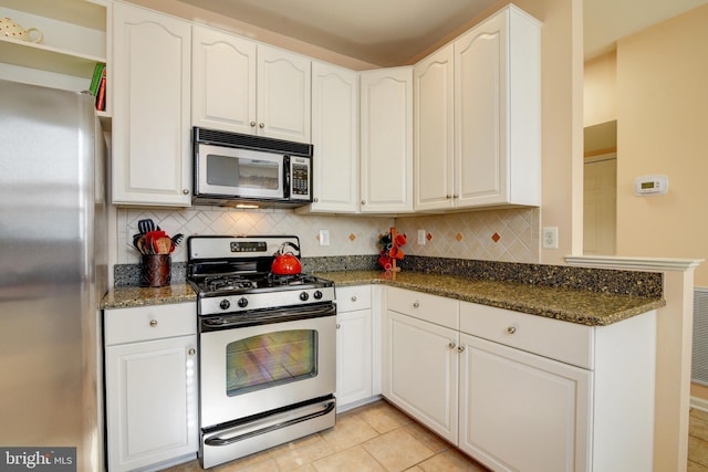 kitchen featuring dark stone counters, stainless steel appliances, a peninsula, and backsplash