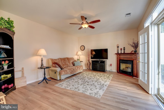 living area featuring light wood finished floors, ceiling fan, visible vents, and a glass covered fireplace