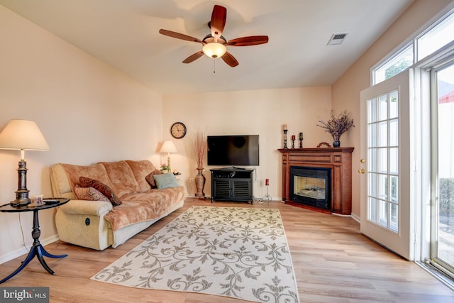 living area with light wood finished floors, a glass covered fireplace, visible vents, and baseboards