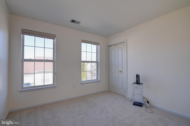 empty room featuring baseboards, visible vents, and light colored carpet