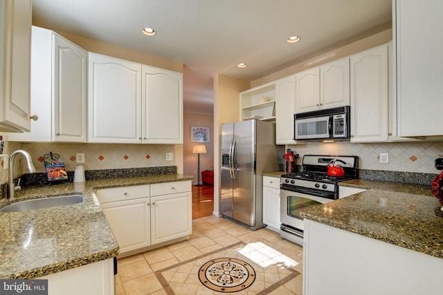 kitchen with dark stone counters, white cabinets, stainless steel appliances, open shelves, and a sink