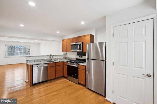 kitchen with brown cabinets, a peninsula, stainless steel appliances, light wood-type flooring, and a sink