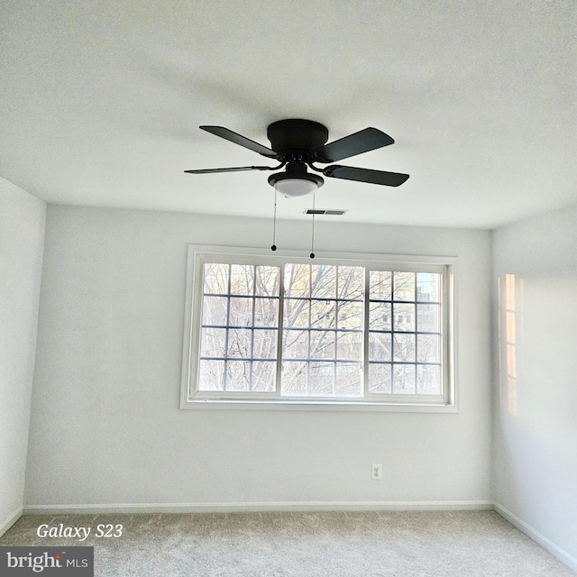 carpeted spare room featuring a ceiling fan, visible vents, and baseboards