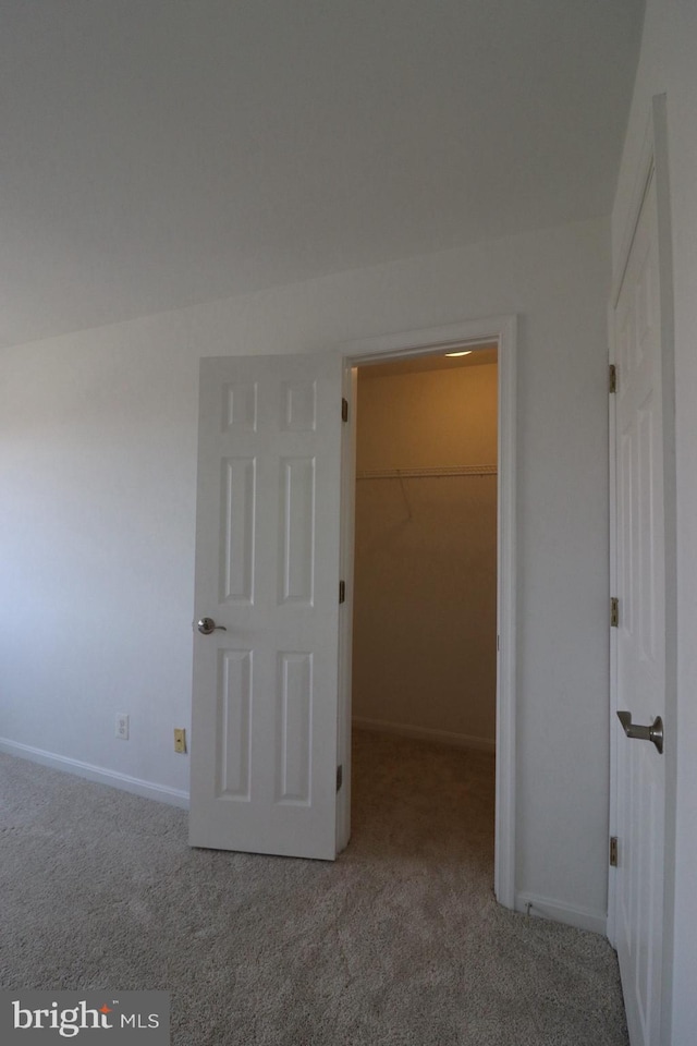 unfurnished bedroom featuring carpet, a spacious closet, baseboards, and a closet