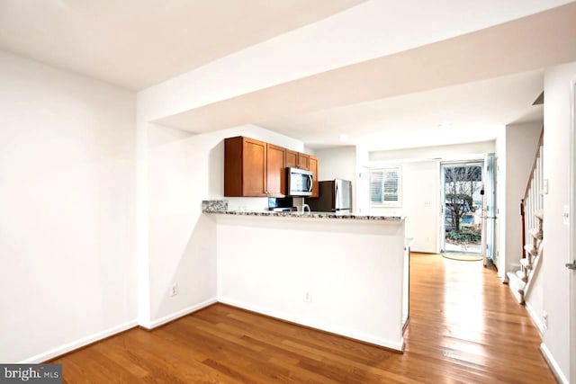 kitchen featuring brown cabinetry, stainless steel microwave, a peninsula, light wood-type flooring, and fridge