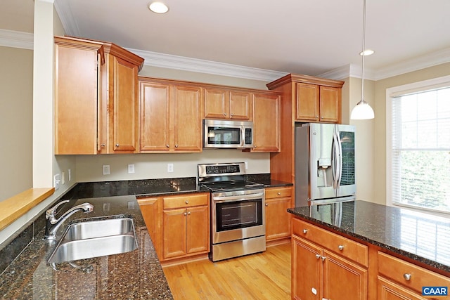 kitchen with stainless steel appliances, a sink, ornamental molding, dark stone counters, and pendant lighting