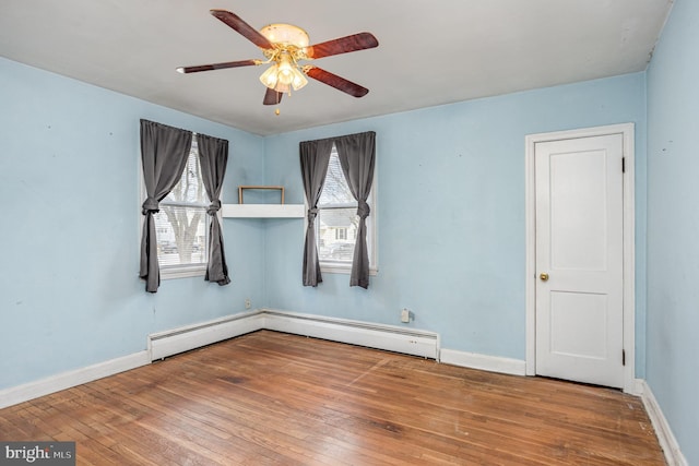 unfurnished room featuring ceiling fan, a baseboard heating unit, wood finished floors, and baseboards