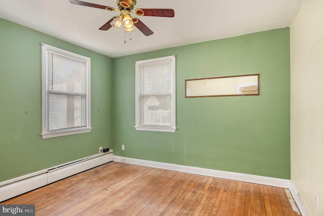 empty room featuring a baseboard heating unit, baseboards, plenty of natural light, and light wood finished floors