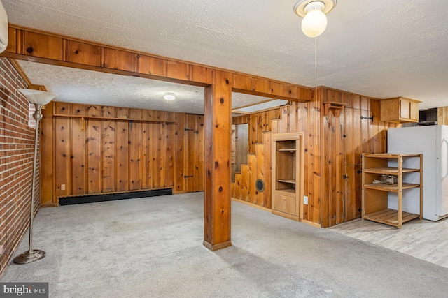 finished basement with brick wall, freestanding refrigerator, a textured ceiling, and light colored carpet