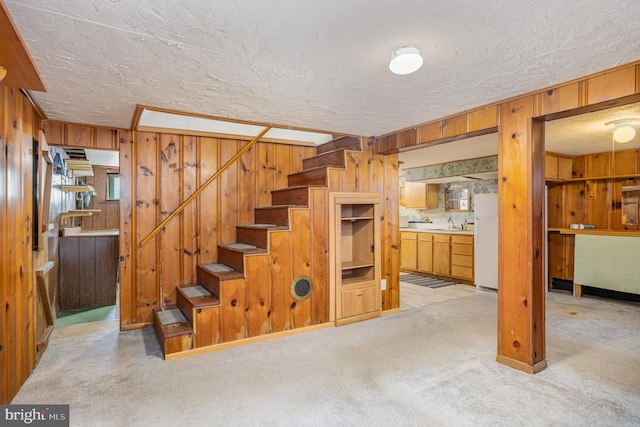 below grade area with wood walls, stairs, a textured ceiling, and freestanding refrigerator