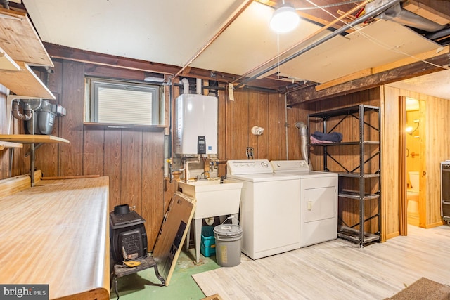 laundry room with laundry area, light wood finished floors, independent washer and dryer, wood walls, and water heater