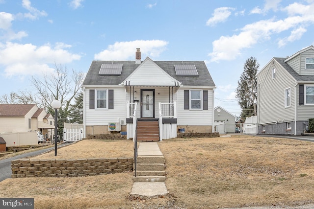 bungalow-style house featuring a chimney, fence, a porch, and roof mounted solar panels