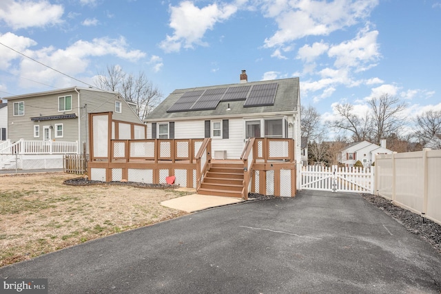 back of house with solar panels, a chimney, stairway, a gate, and a wooden deck