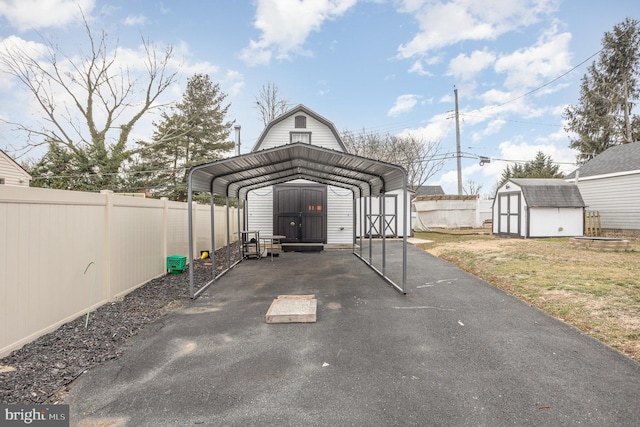 view of parking / parking lot featuring a carport, a storage unit, fence, and aphalt driveway