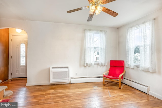 sitting room with arched walkways, a baseboard radiator, light wood-style flooring, a ceiling fan, and baseboards