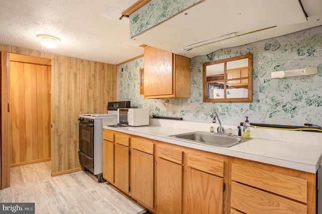 kitchen featuring light countertops, light wood-style flooring, stove, a sink, and wallpapered walls