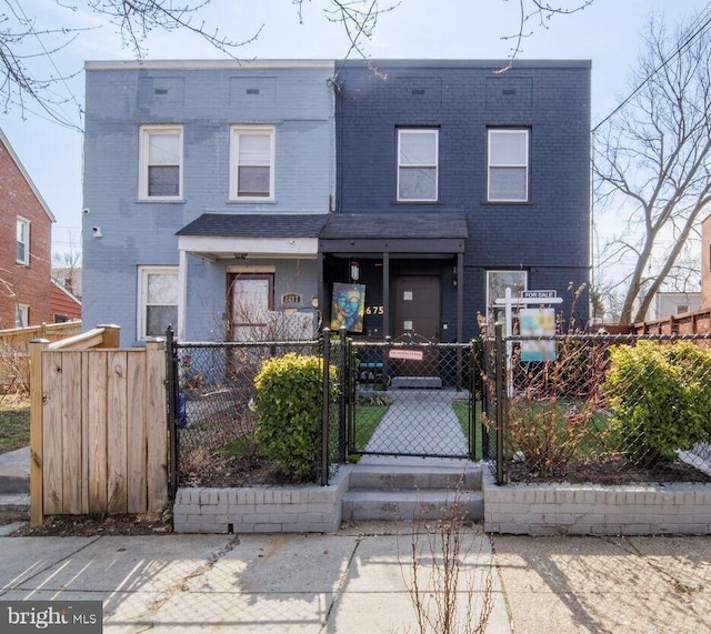 multi unit property featuring a fenced front yard, a gate, and brick siding