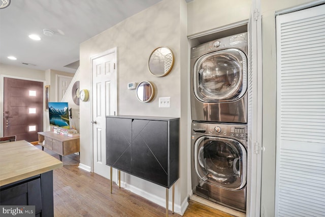 laundry area featuring recessed lighting, laundry area, stacked washer / dryer, wood finished floors, and baseboards