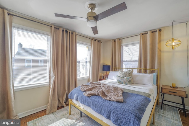 bedroom with ceiling fan, multiple windows, wood finished floors, and baseboards