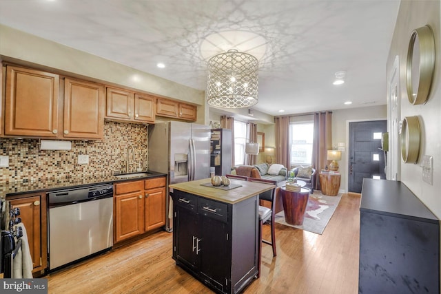 kitchen with appliances with stainless steel finishes, light wood-type flooring, a sink, and decorative backsplash