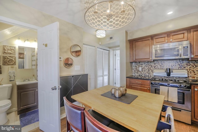 kitchen featuring brown cabinets, dark countertops, backsplash, appliances with stainless steel finishes, and a sink