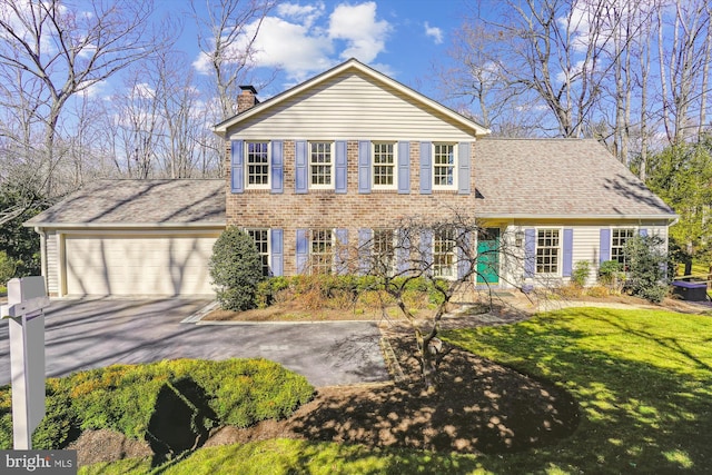 view of front of property featuring a chimney, aphalt driveway, an attached garage, a front yard, and brick siding