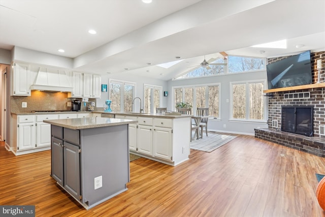 kitchen with a fireplace, white cabinetry, open floor plan, a center island, and lofted ceiling with skylight