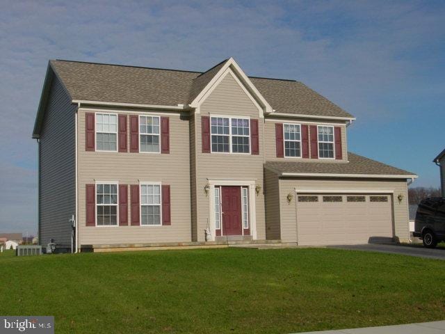 colonial home featuring driveway, an attached garage, and a front yard