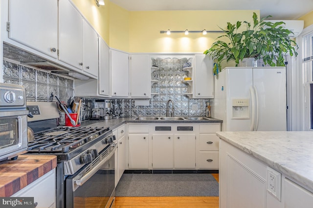 kitchen featuring white refrigerator with ice dispenser, a sink, white cabinetry, backsplash, and gas stove