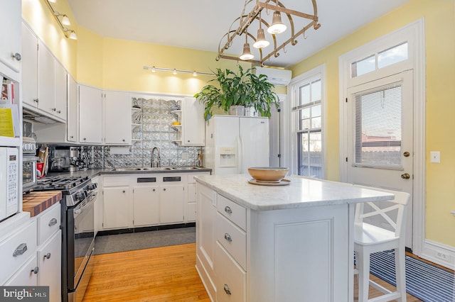 kitchen featuring white refrigerator with ice dispenser, white cabinets, stainless steel gas range oven, and a wall mounted AC