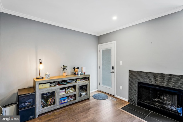 living area with a tile fireplace, visible vents, baseboards, dark wood-style floors, and crown molding