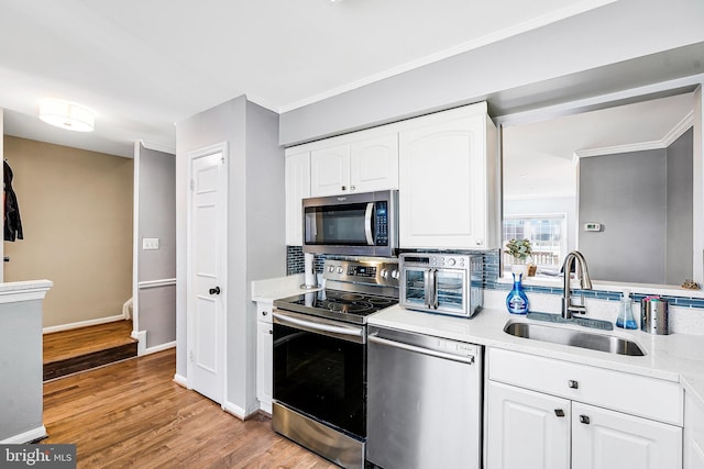 kitchen with white cabinets, a sink, stainless steel appliances, light wood-type flooring, and backsplash