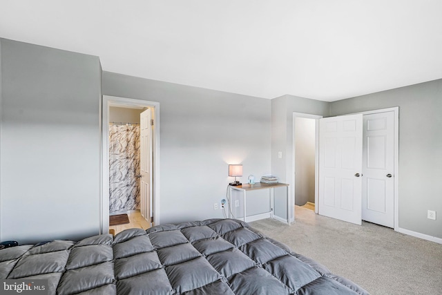 bedroom with light colored carpet, baseboards, and ensuite bathroom