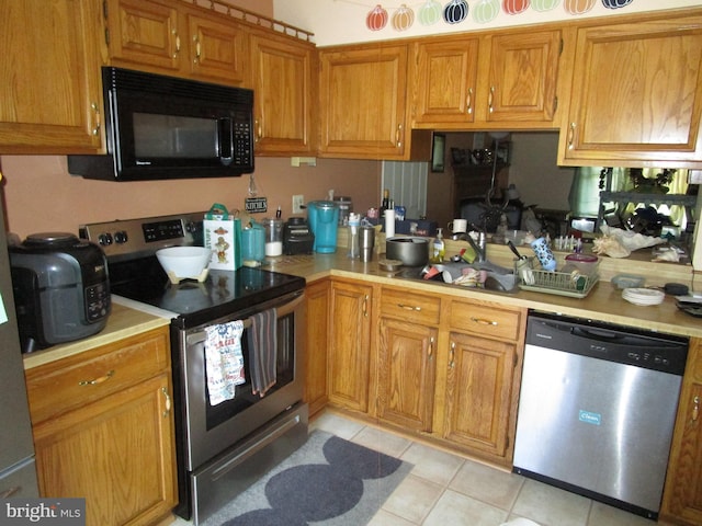 kitchen featuring appliances with stainless steel finishes, brown cabinets, light countertops, and light tile patterned floors