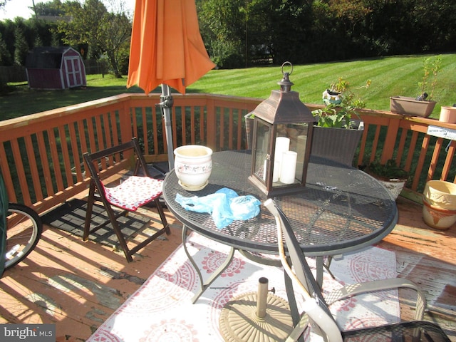 deck with a storage unit, an outbuilding, a lawn, and outdoor dining space