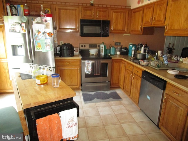 kitchen featuring brown cabinets, light tile patterned floors, stainless steel appliances, wooden counters, and a sink