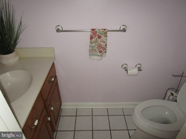 half bath with toilet, tile patterned floors, baseboards, and vanity