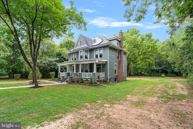 view of front of home with covered porch, driveway, roof mounted solar panels, a front lawn, and a chimney