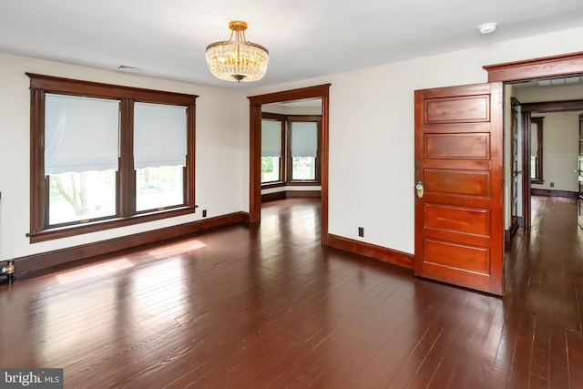 empty room featuring baseboards, visible vents, a chandelier, and dark wood-style flooring